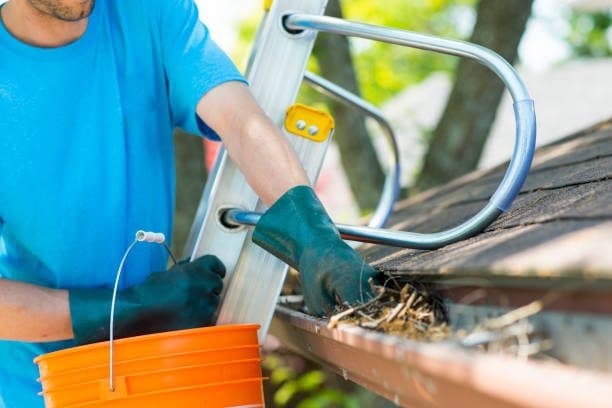 Worker clearing leaves and debris from house gutters